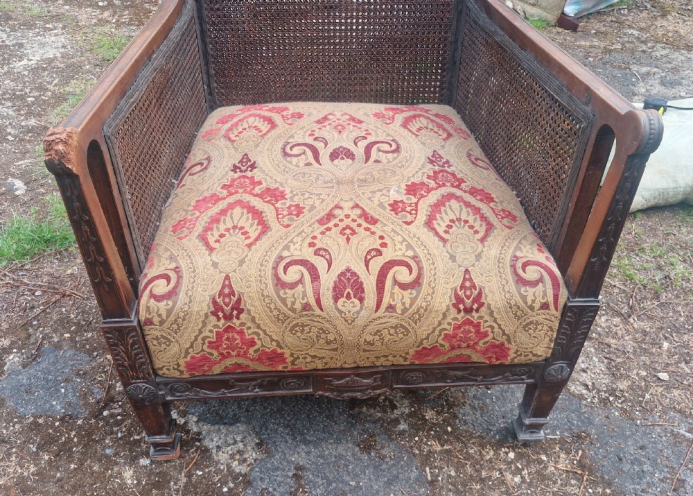 An Edwardian mahogany bergere armchair with woven cane panels on the back and sides and a patterned upholstery seat cushion. View V