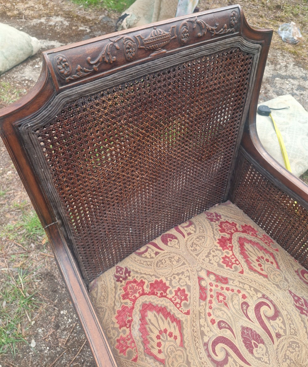 An Edwardian mahogany bergere armchair with woven cane panels on the back and sides and a patterned upholstery seat cushion. View VI