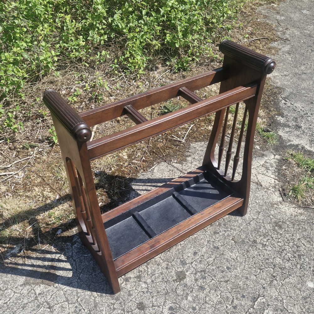 A late Victorian mahogany umbrella and stick stand featuring turned side spindles, reeded end handles, divided upper sections, and a black cast iron drip tray. View VII