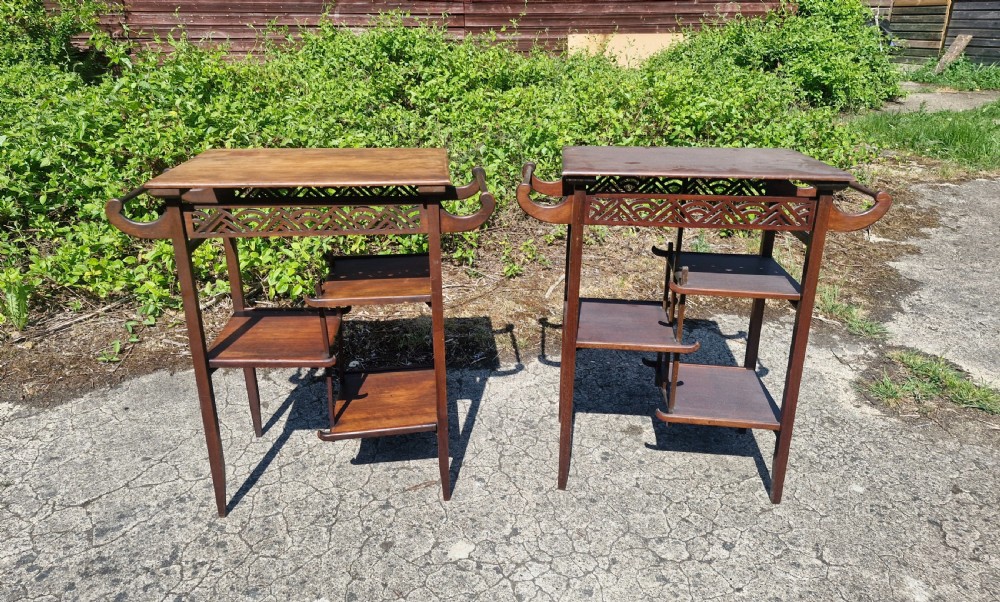 A pair of mahogany Anglo-Japanese occasional tables featuring pierced fretwork friezes, side handles, and staggered lower shelves.