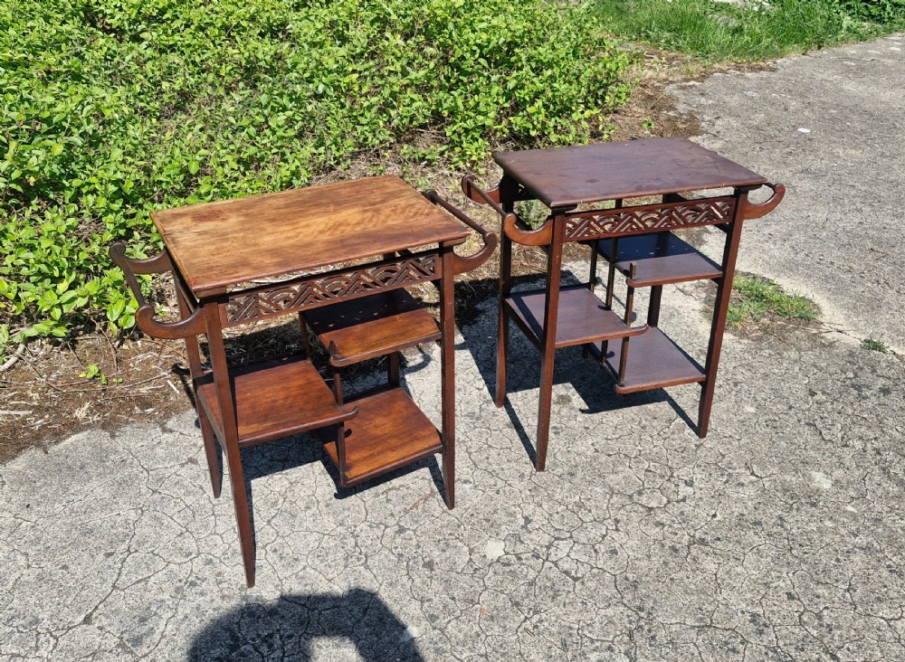 A pair of mahogany Anglo-Japanese occasional tables featuring pierced fretwork friezes, side handles, and staggered lower shelves. View X