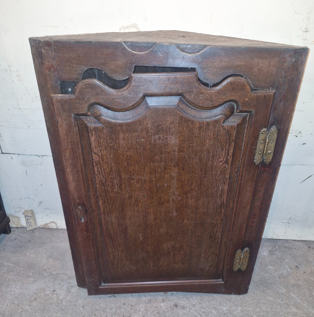 An antique dark oak French corner cupboard featuring a single carved panelled door with brass hinges and a shaped top outline. View II