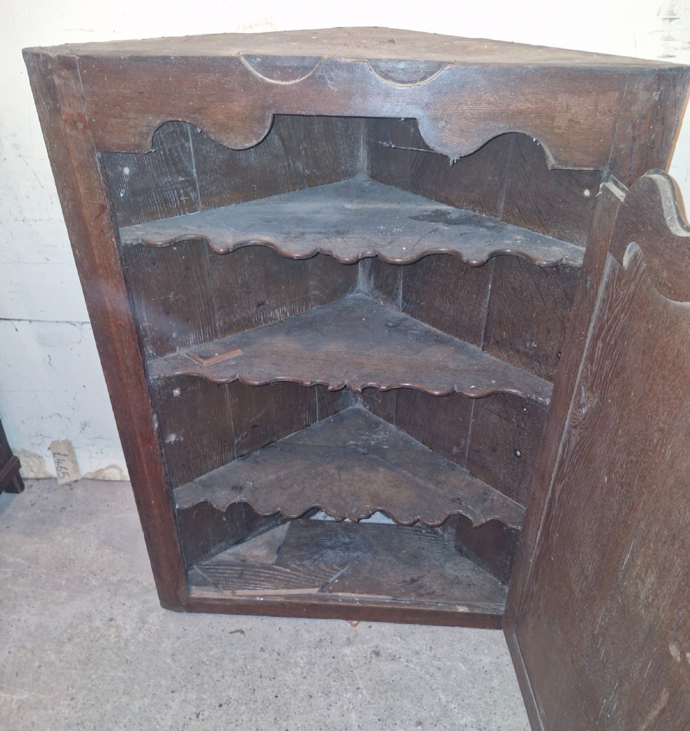 An antique dark oak French corner cupboard featuring a single carved panelled door with brass hinges and a shaped top outline. View IV