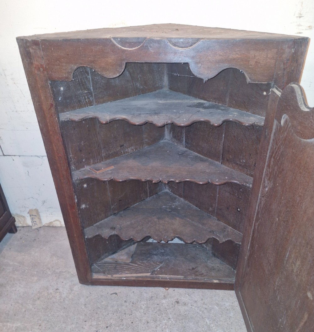 An antique dark oak French corner cupboard featuring a single carved panelled door with brass hinges and a shaped top outline. View V