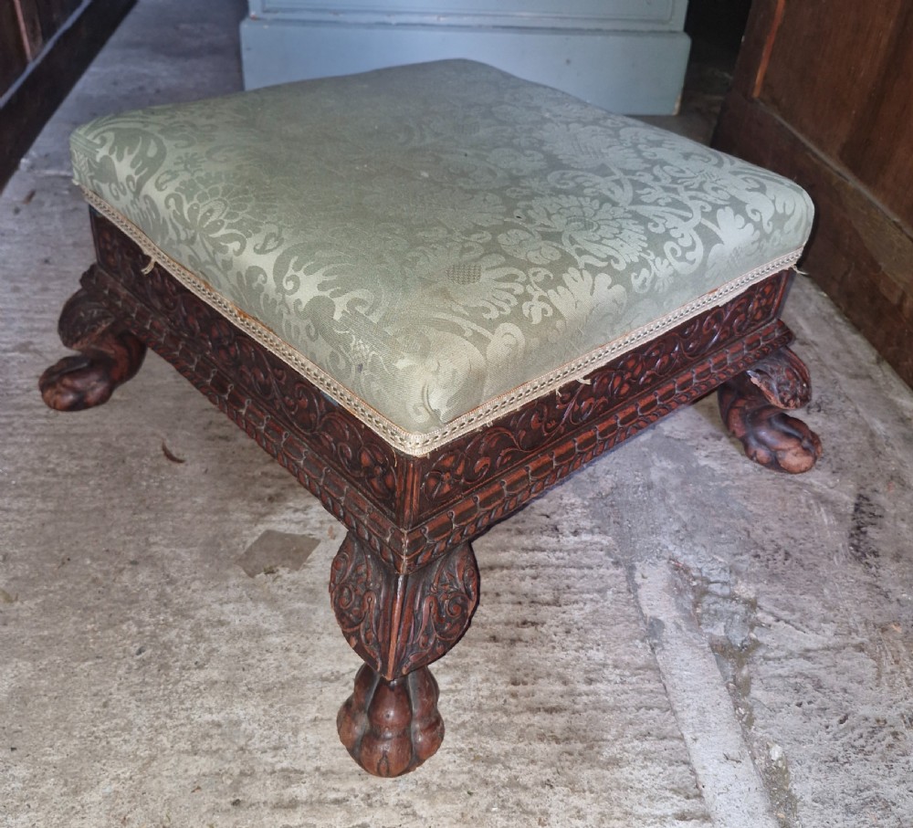 A square Anglo-Indian footstool featuring a green damask upholstered top above a deeply carved dark hardwood frame with claw feet. View II