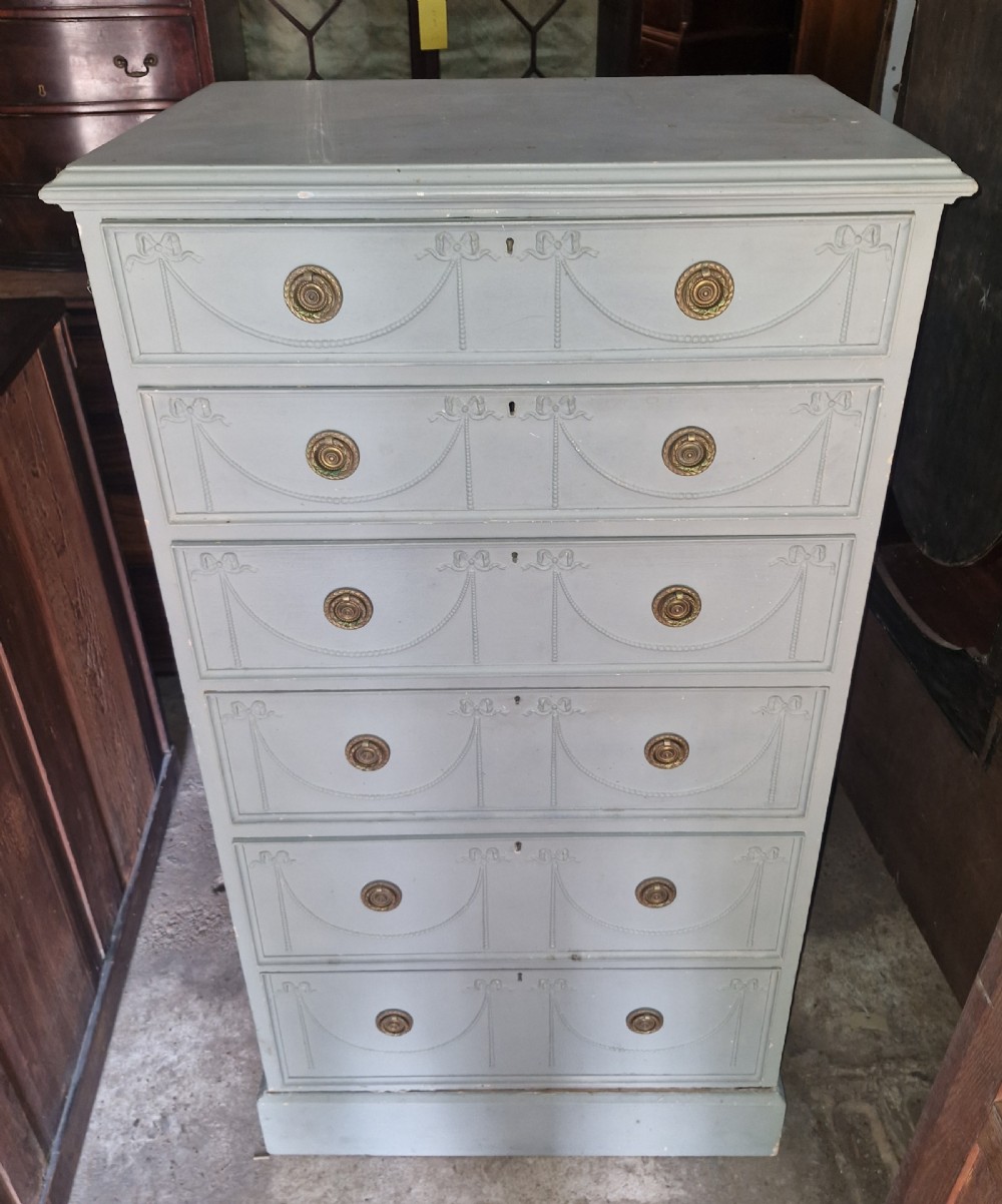 An Edwardian light grey painted pine Wellington chest featuring six drawers decorated with carved ribbon swag details and brass ring handles. View III