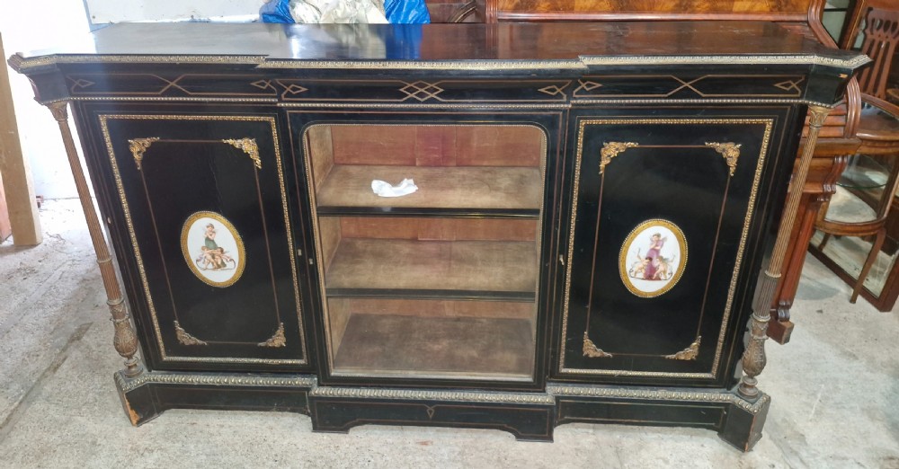 A Victorian ebonised three-door credenza featuring a central glazed compartment flanked by panelled doors decorated with oval hand-painted porcelain plaques and gilt metal mounts.
