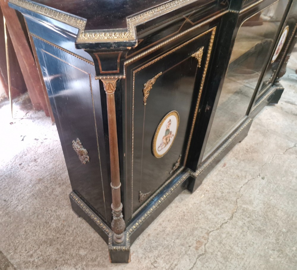 A Victorian ebonised three-door credenza featuring a central glazed compartment flanked by panelled doors decorated with oval hand-painted porcelain plaques and gilt metal mounts. View VIII