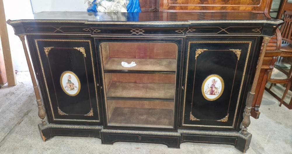 A Victorian ebonised three-door credenza featuring a central glazed compartment flanked by panelled doors decorated with oval hand-painted porcelain plaques and gilt metal mounts. View IX