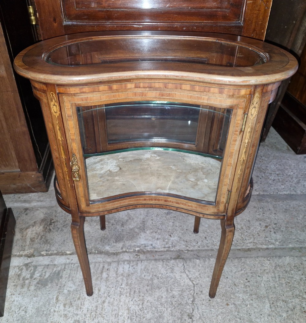 An Edwardian kidney-shaped mahogany bijouterie display cabinet featuring glass panels, marquetry inlay, and cabriole legs.