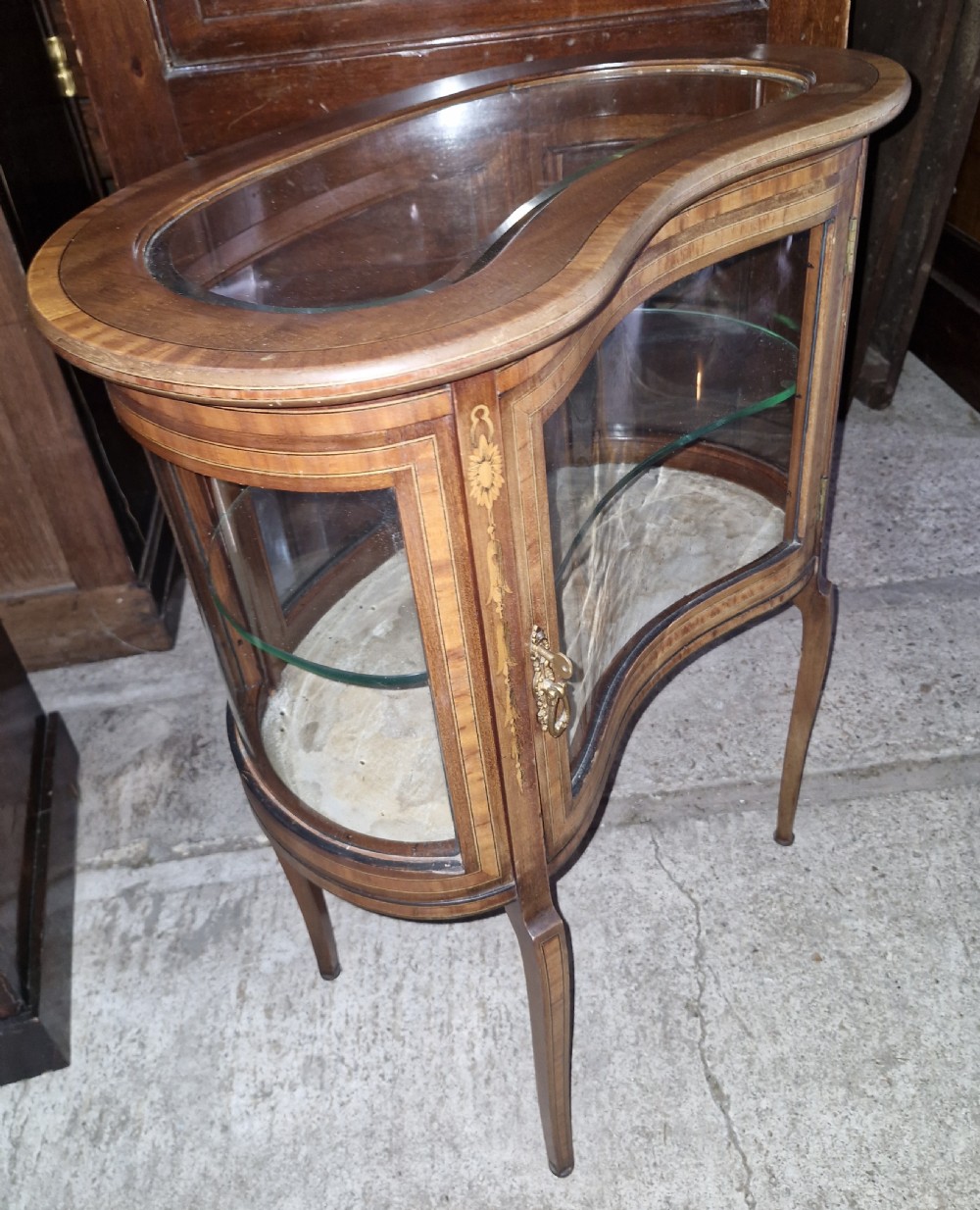 An Edwardian kidney-shaped mahogany bijouterie display cabinet featuring glass panels, marquetry inlay, and cabriole legs. View V