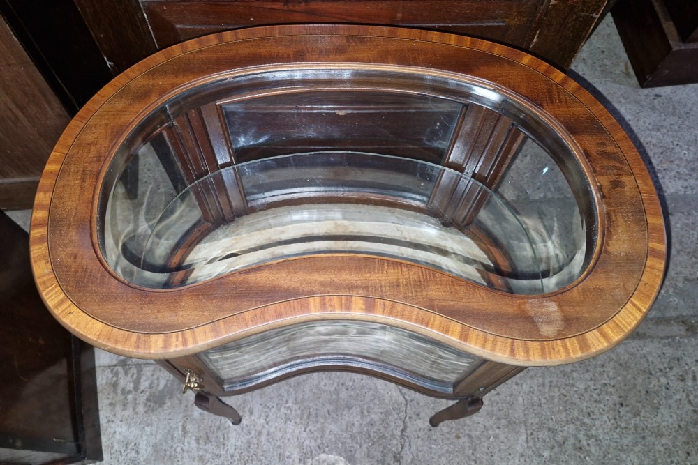 An Edwardian kidney-shaped mahogany bijouterie display cabinet featuring glass panels, marquetry inlay, and cabriole legs. View VI