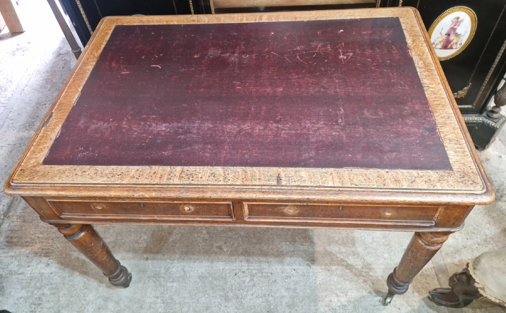 A Victorian oak writing table featuring an inset leather writing surface, two frieze drawers, turned legs, and brass castors. View II