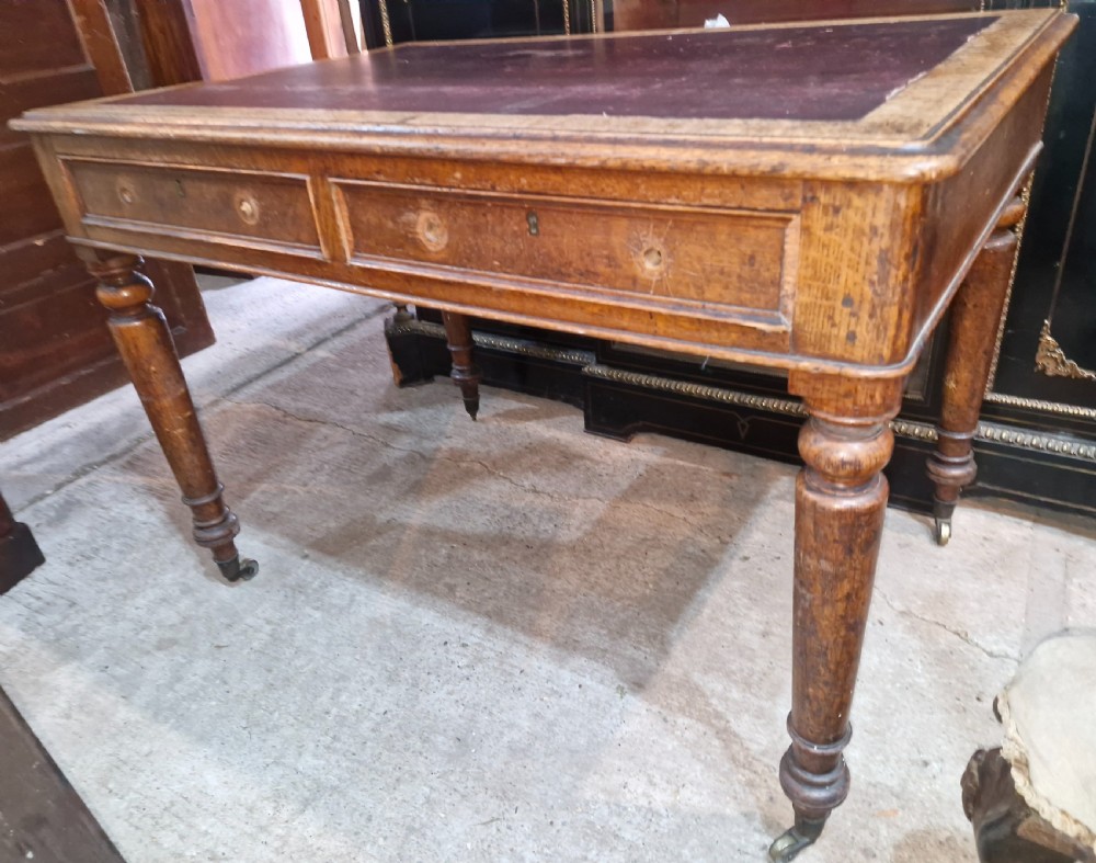 A Victorian oak writing table featuring an inset leather writing surface, two frieze drawers, turned legs, and brass castors.