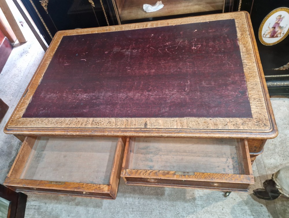 A Victorian oak writing table featuring an inset leather writing surface, two frieze drawers, turned legs, and brass castors. View V