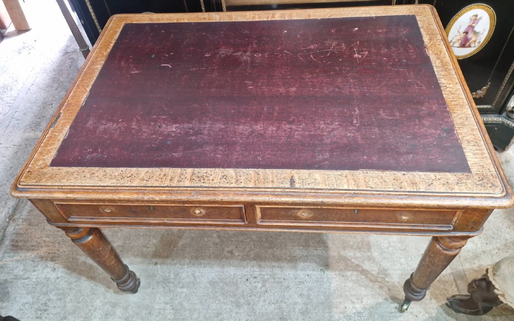A Victorian oak writing table featuring an inset leather writing surface, two frieze drawers, turned legs, and brass castors. View VI