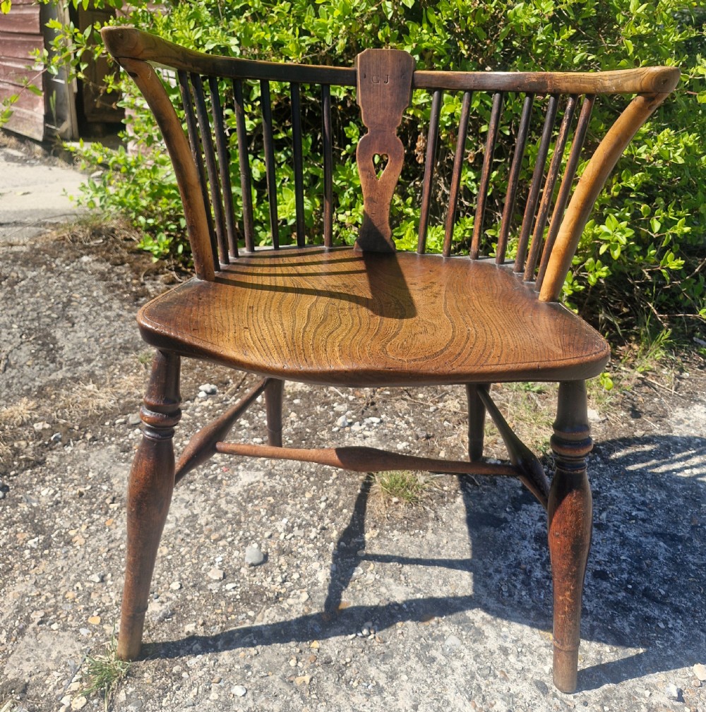 A mid 19th-century wooden Windsor desk armchair with a shaped saddle seat, spindle back with carved heart central splat, and turned legs.