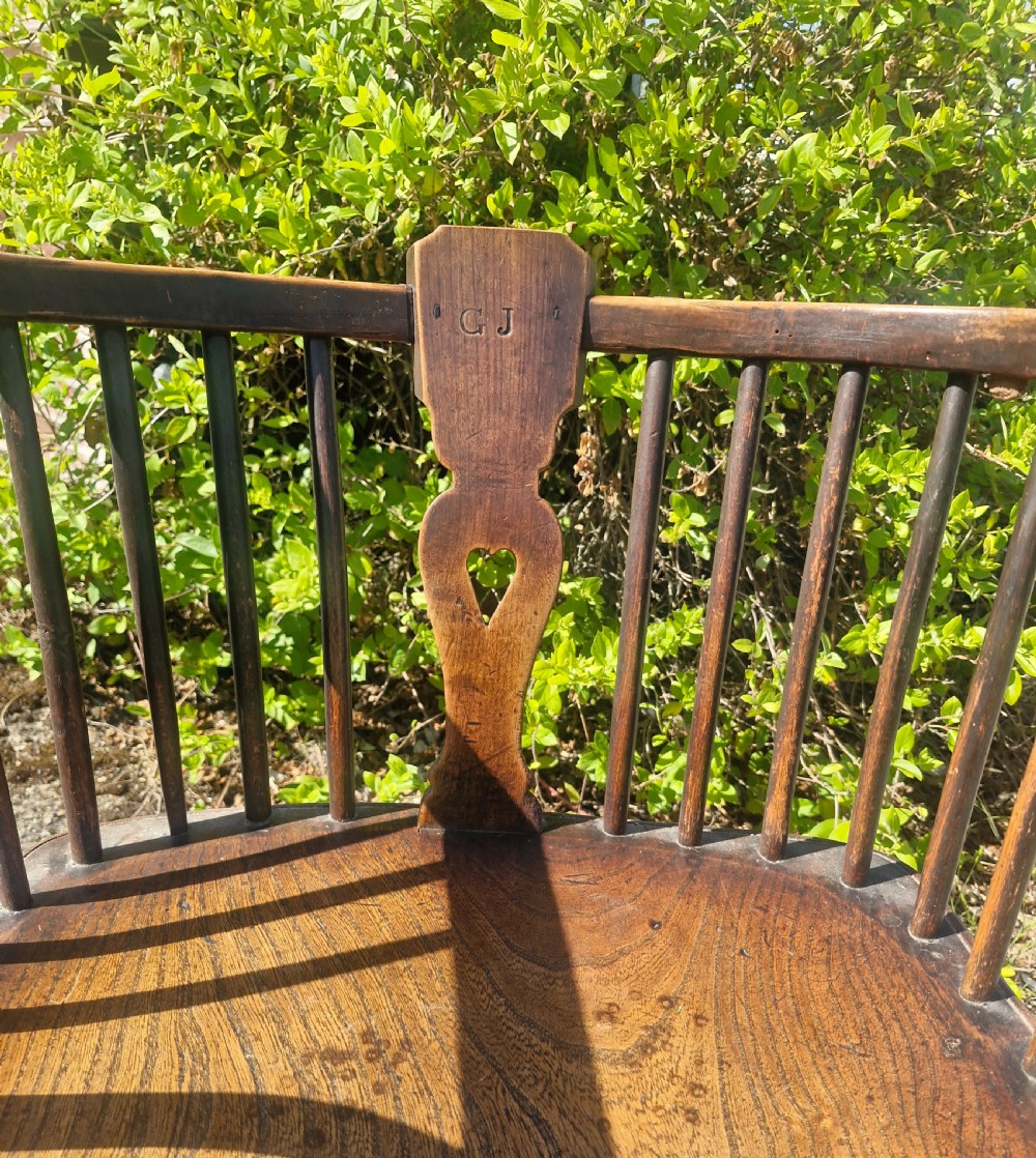 A mid 19th-century wooden Windsor desk armchair with a shaped saddle seat, spindle back with carved heart central splat, and turned legs. View IV