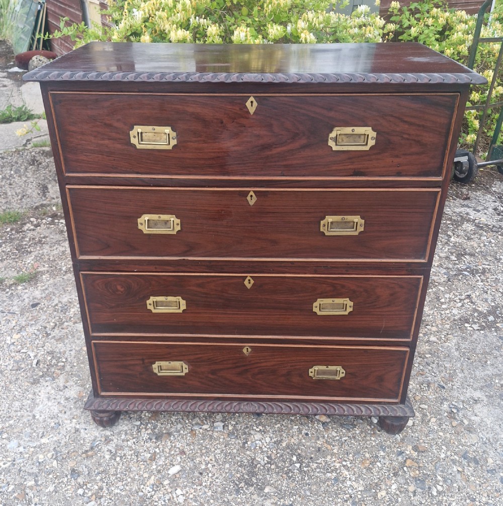 A four-drawer dark rosewood Anglo-Indian campaign secretaire chest featuring recessed brass handles, diamond escutcheons, and carved gadrooned borders.