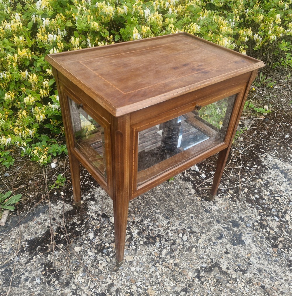 An Edwardian mahogany tea trolley featuring drop-down glazed side panels, satinwood string inlay, tapered legs, and small brass castors.
