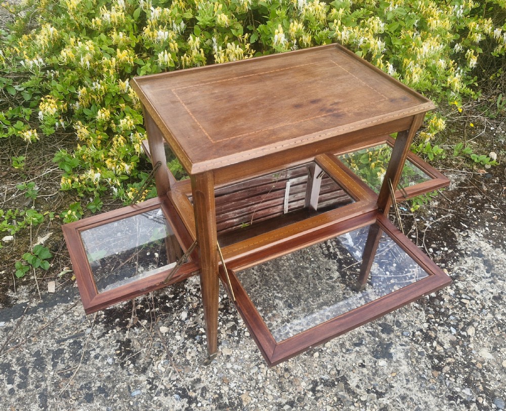 An Edwardian mahogany tea trolley featuring drop-down glazed side panels, satinwood string inlay, tapered legs, and small brass castors. View II