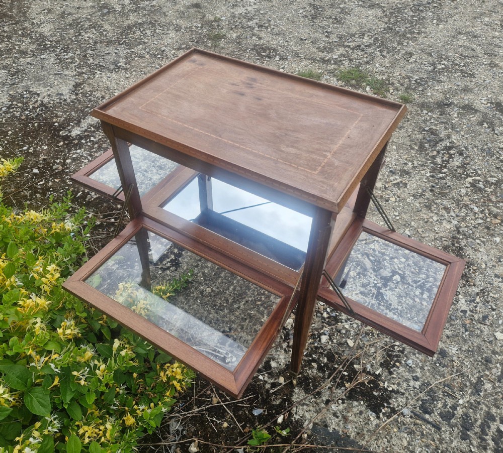 An Edwardian mahogany tea trolley featuring drop-down glazed side panels, satinwood string inlay, tapered legs, and small brass castors. View V