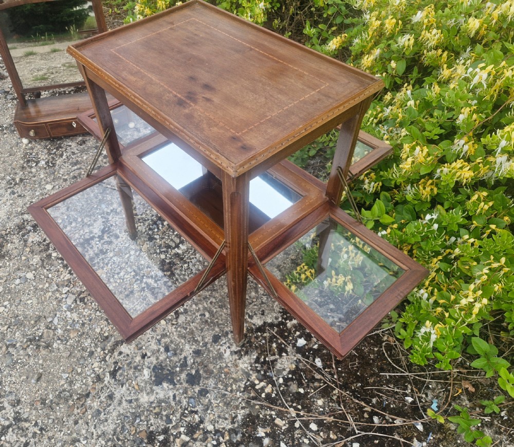 An Edwardian mahogany tea trolley featuring drop-down glazed side panels, satinwood string inlay, tapered legs, and small brass castors. View VI