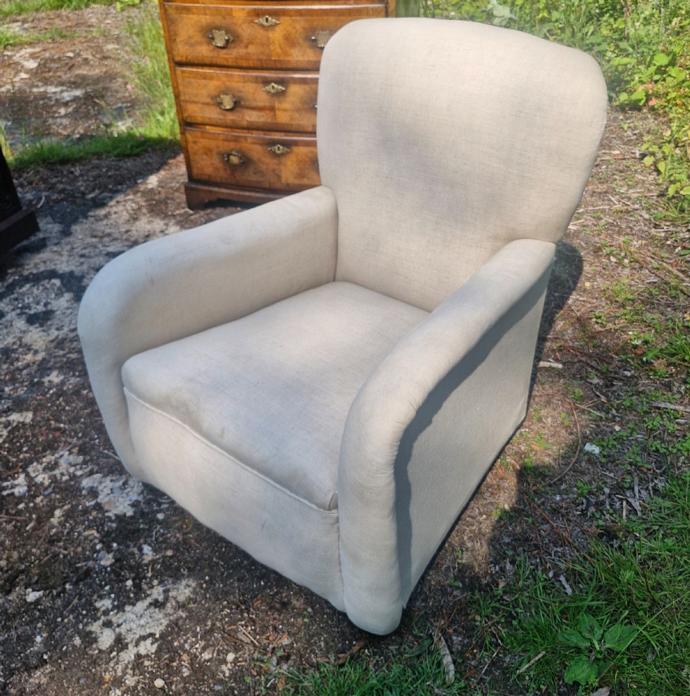 A fully upholstered early 20th century childs armchair featuring neutral beige fabric, rolled arms, and a curved backrest. View II