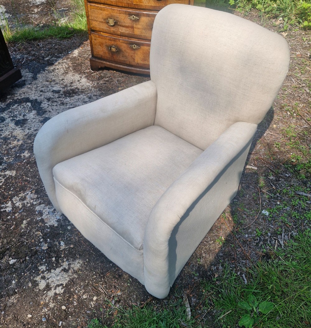 A fully upholstered early 20th century childs armchair featuring neutral beige fabric, rolled arms, and a curved backrest. View III