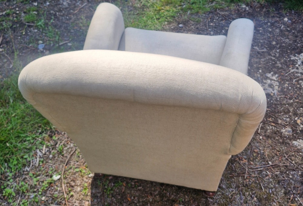 A fully upholstered early 20th century childs armchair featuring neutral beige fabric, rolled arms, and a curved backrest. View V