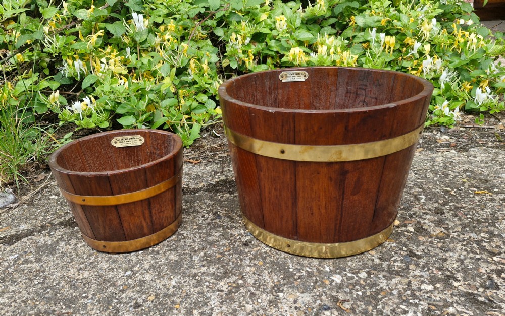 A pair of graduated tapered wooden planters constructed with coopered staves and bound with polished brass bands.