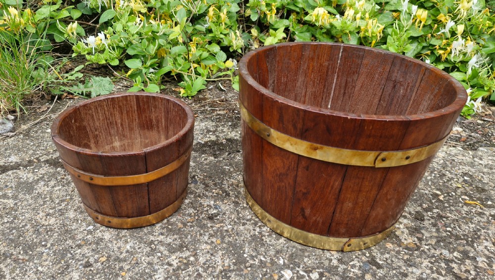 A pair of graduated tapered wooden planters constructed with coopered staves and bound with polished brass bands. View IV