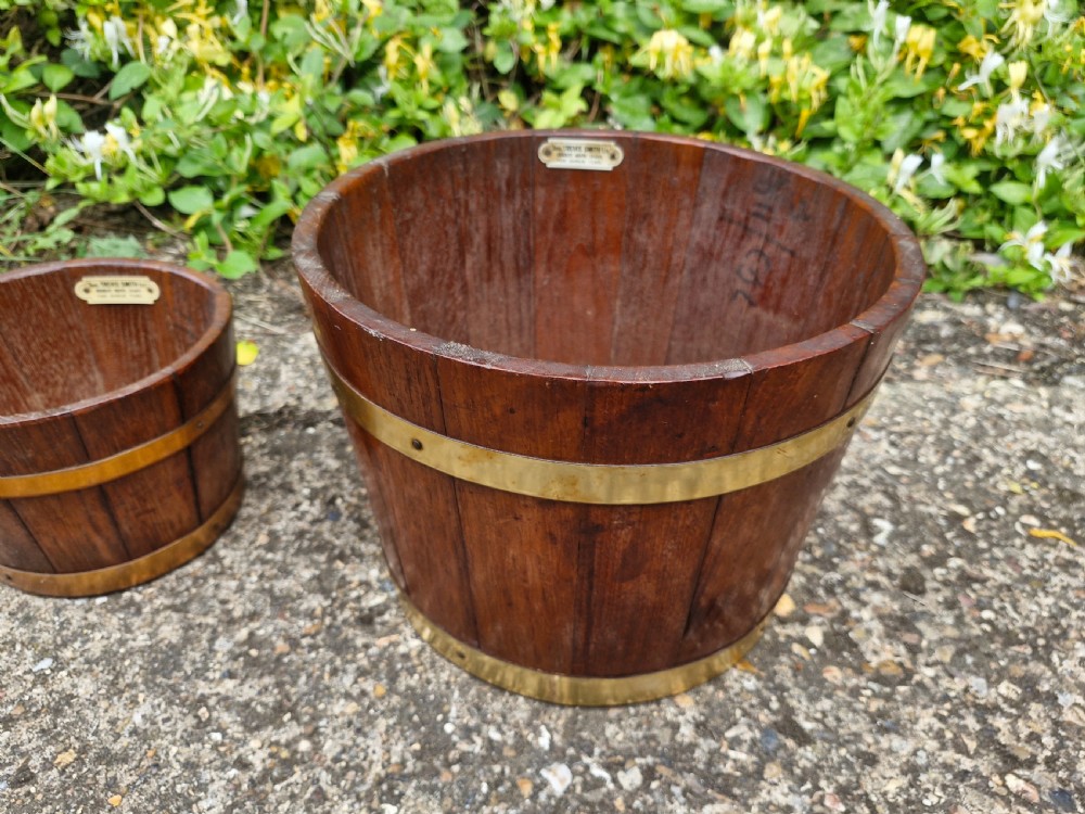 A pair of graduated tapered wooden planters constructed with coopered staves and bound with polished brass bands. View V