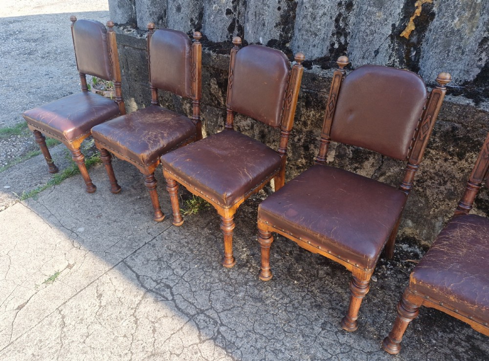 A set of eight Victorian oak dining chairs with brown leather upholstery, brass stud trim, turned legs, and carved frame details. View IX
