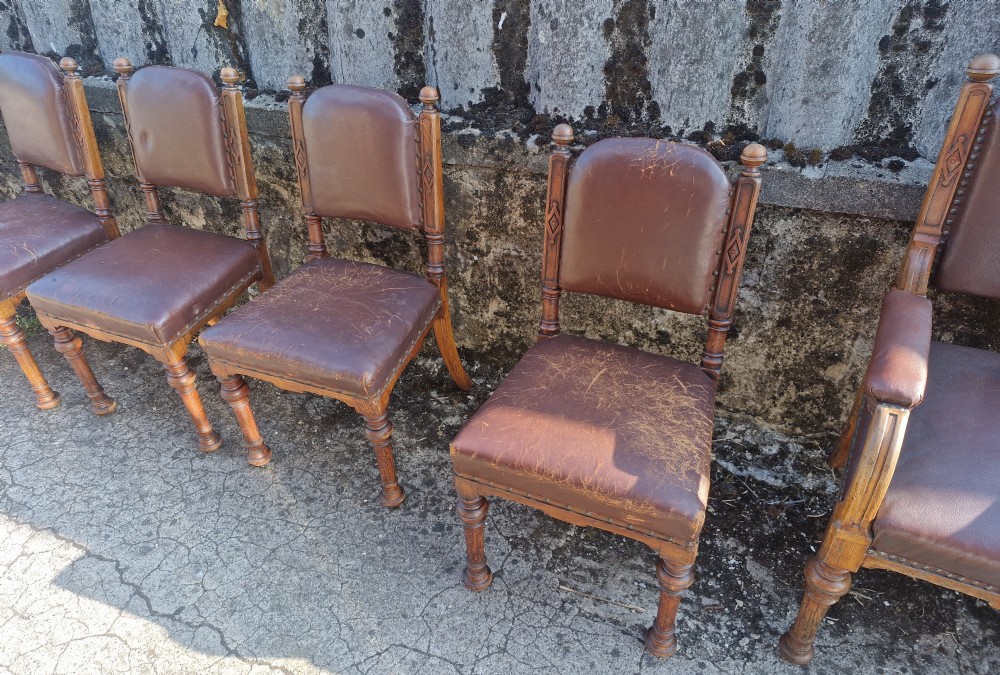 A set of eight Victorian oak dining chairs with brown leather upholstery, brass stud trim, turned legs, and carved frame details. View X