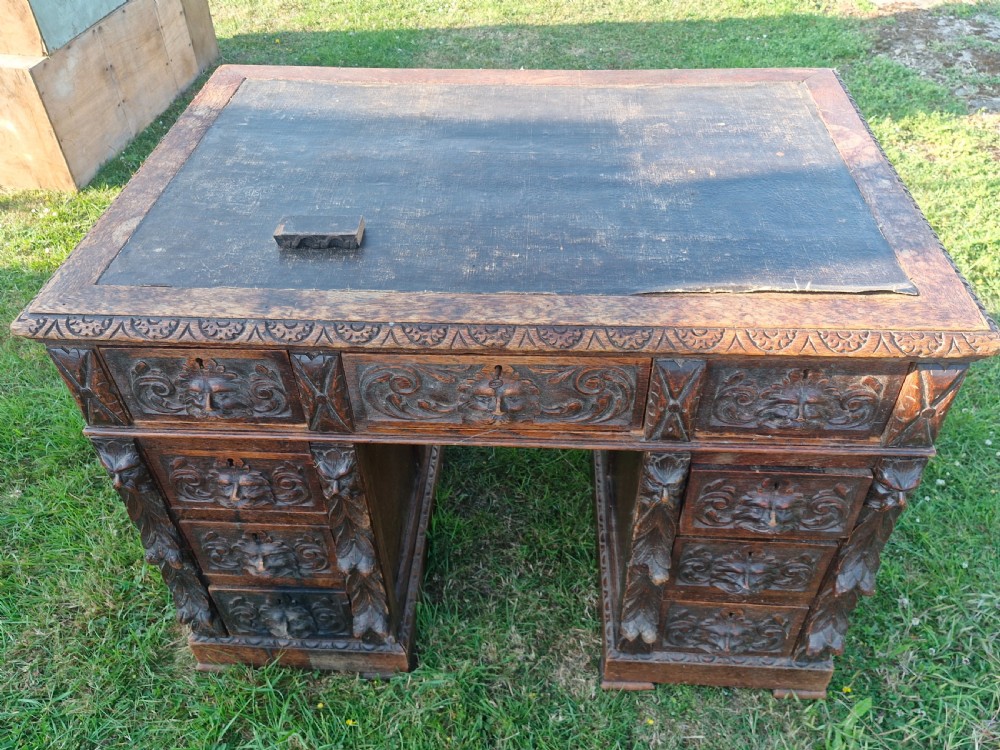 A carved dark oak twin-pedestal desk featuring relief mask drawer handles, foliate side columns, and an inset dark leather writing surface.