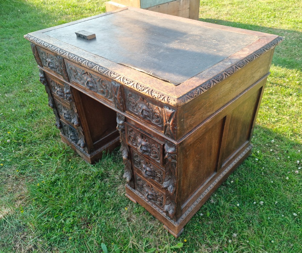 A carved dark oak twin-pedestal desk featuring relief mask drawer handles, foliate side columns, and an inset dark leather writing surface. View II