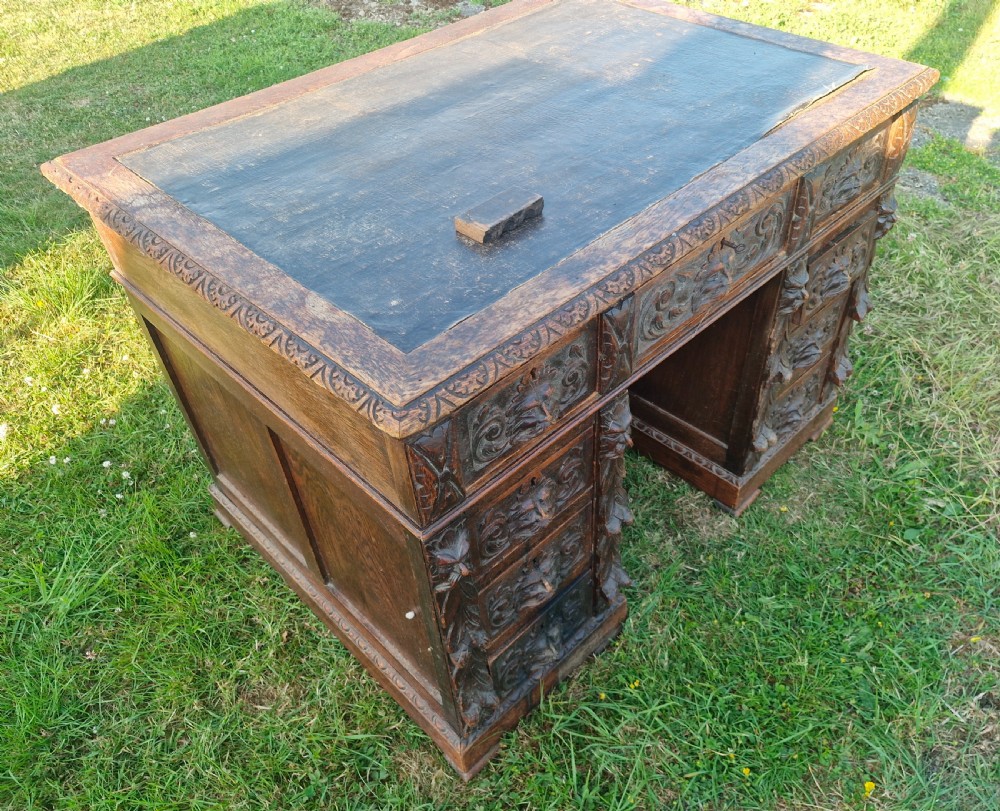 A carved dark oak twin-pedestal desk featuring relief mask drawer handles, foliate side columns, and an inset dark leather writing surface. View III