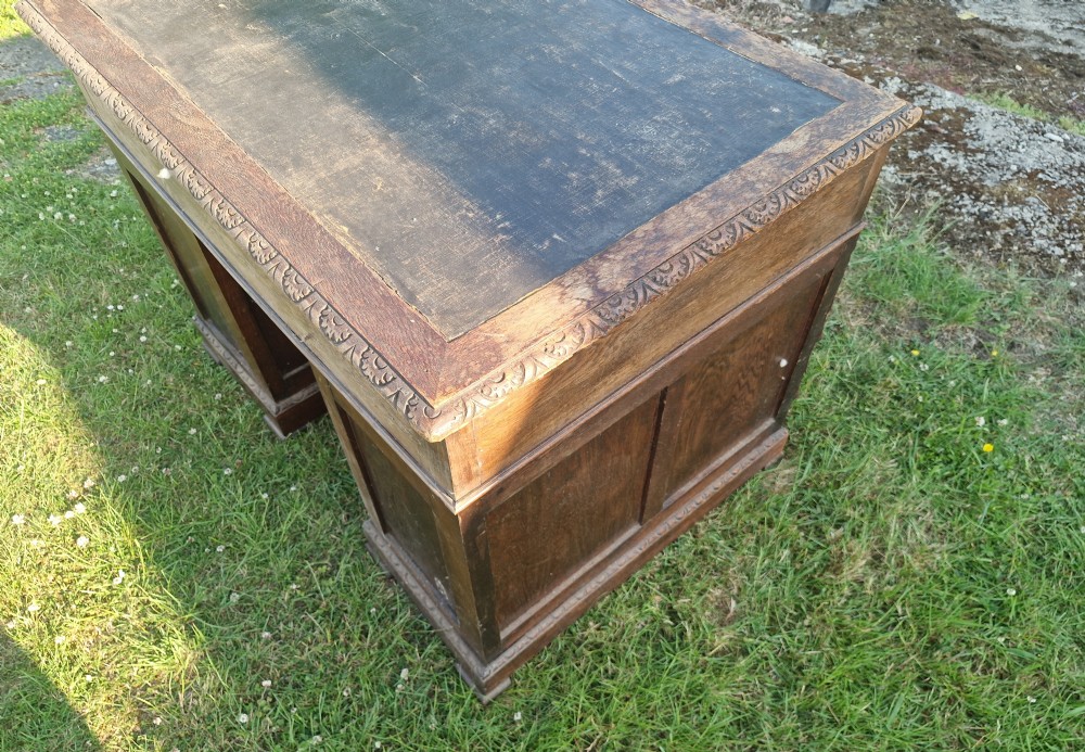 A carved dark oak twin-pedestal desk featuring relief mask drawer handles, foliate side columns, and an inset dark leather writing surface. View VII