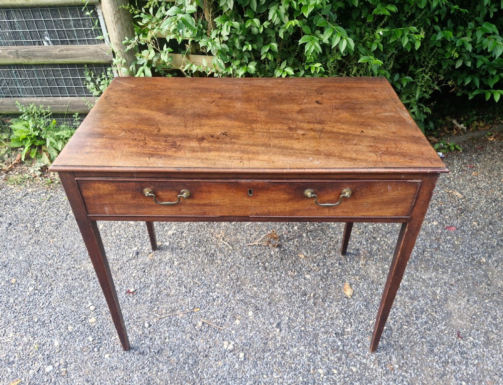 A late Georgian mahogany side table featuring a single long drawer with two brass swan-neck handles and four square tapered legs. View II