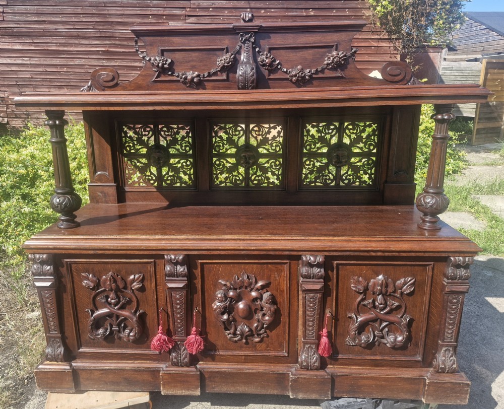 An ornate dark oak Victorian buffet featuring relief-carved cabinet doors, turned support columns, openwork fretwork back panels, and an arched top pediment with carved swag detailing.