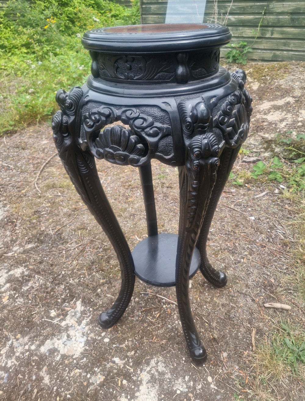 An early 20th-century ebonised hardwood Oriental jardiniere stand with carved aprons, cabriole legs, and a lower shelf.