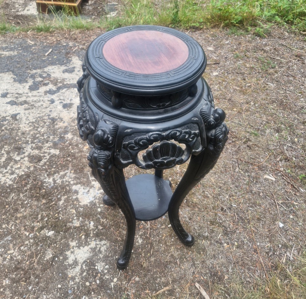 An early 20th-century ebonised hardwood Oriental jardiniere stand with carved aprons, cabriole legs, and a lower shelf. View V