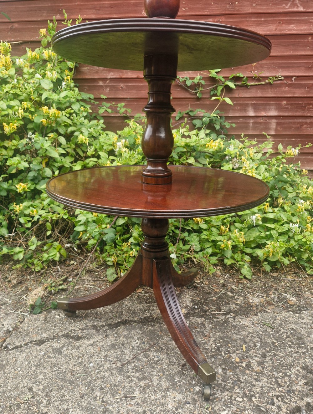 A three-tiered Regency mahogany dumb waiter featuring circular trays supported by turned columns and standing on reeded legs with brass castors. View IV