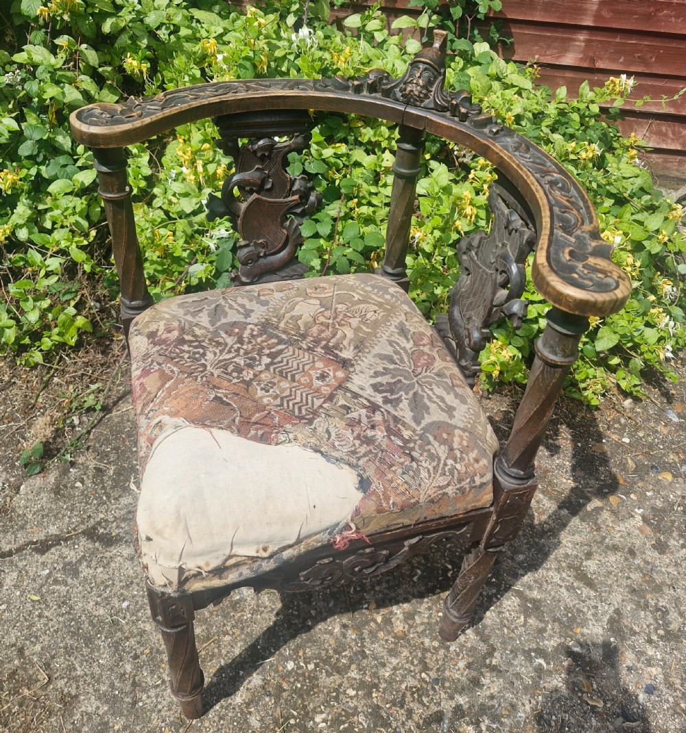 A late 19th-century carved oak corner armchair featuring a curved crest rail with a carved mask detail, turned supports, and a tapestry upholstered seat.