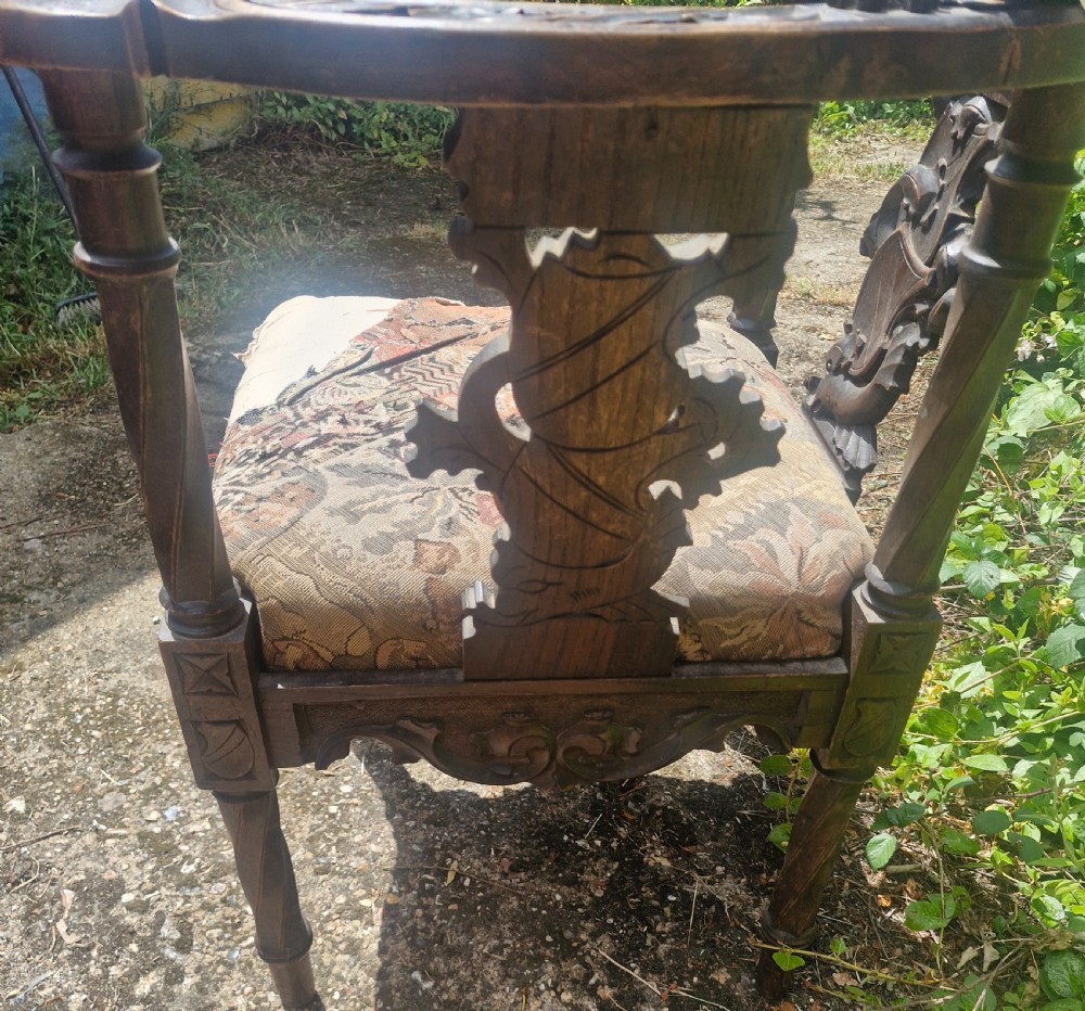 A late 19th-century carved oak corner armchair featuring a curved crest rail with a carved mask detail, turned supports, and a tapestry upholstered seat. View II
