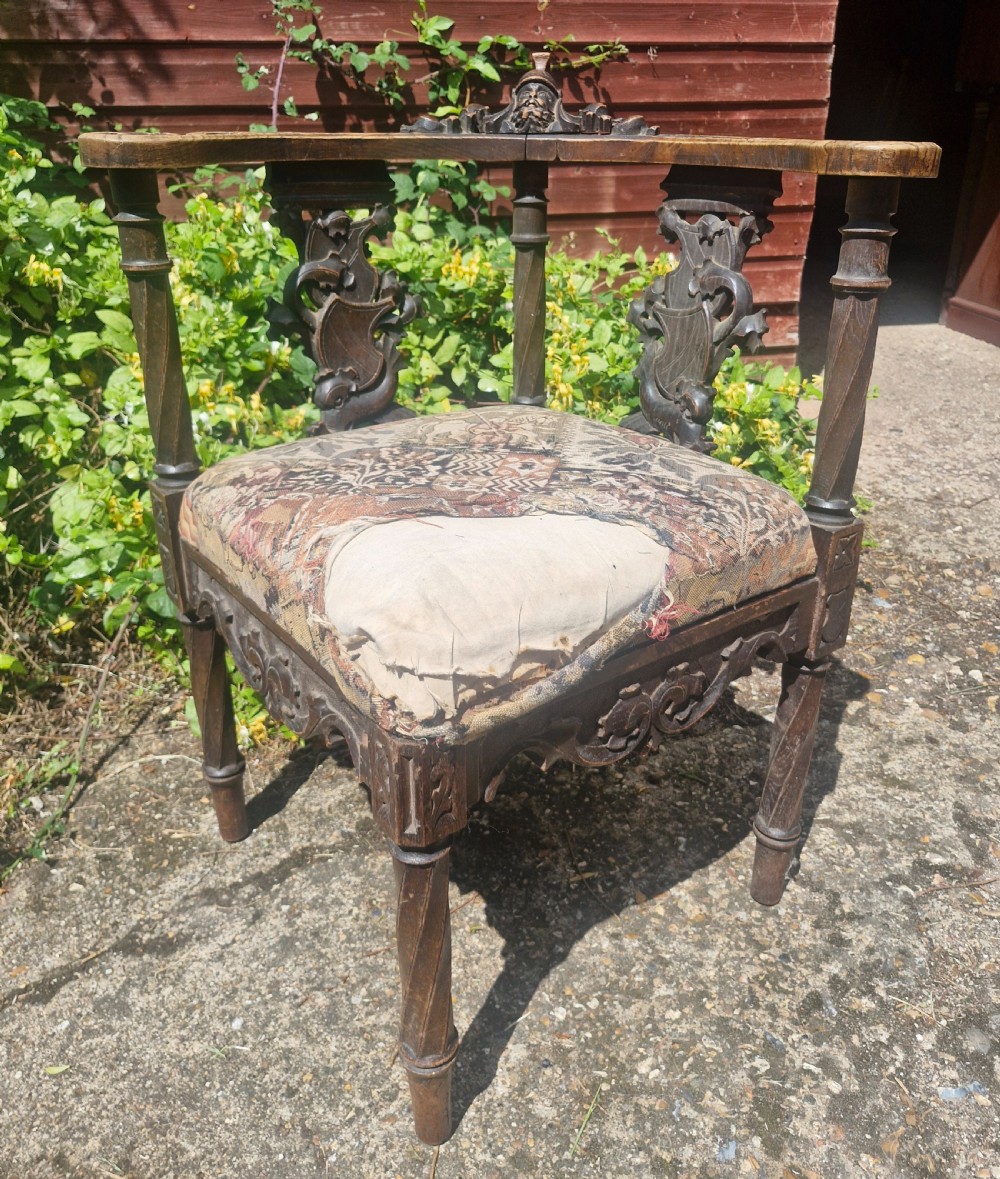 A late 19th-century carved oak corner armchair featuring a curved crest rail with a carved mask detail, turned supports, and a tapestry upholstered seat. View IV