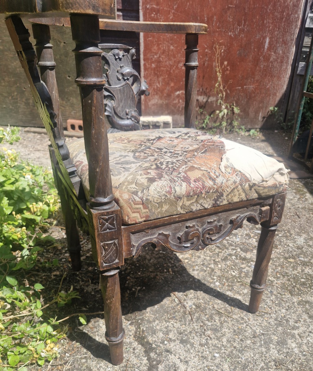 A late 19th-century carved oak corner armchair featuring a curved crest rail with a carved mask detail, turned supports, and a tapestry upholstered seat. View V