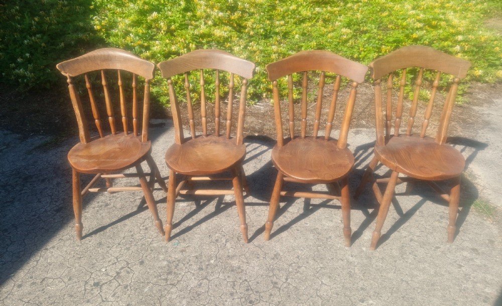 A set of four early twentieth century wooden farmhouse kitchen chairs with spindle backs and carved saddle seats.