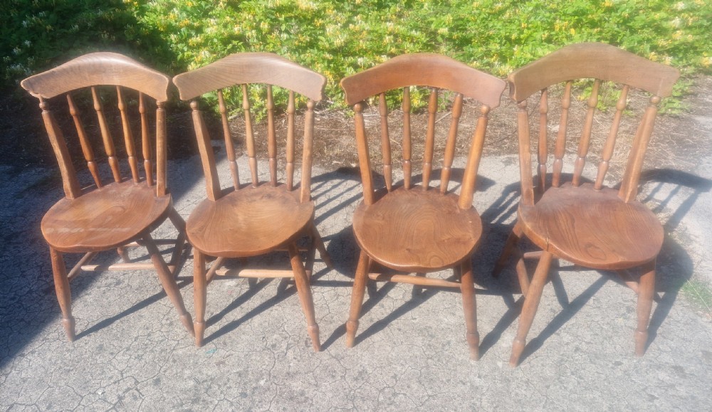 A set of four early twentieth century wooden farmhouse kitchen chairs with spindle backs and carved saddle seats. View II